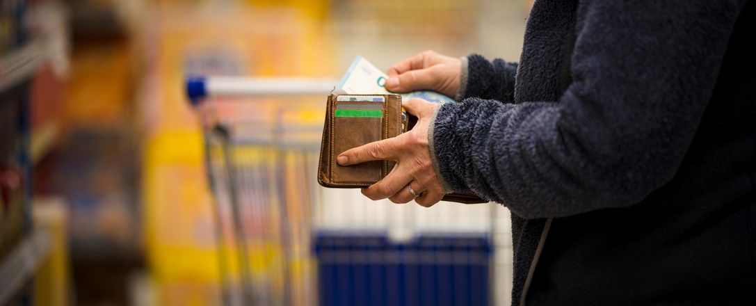 Eine Person steht mit einem Portemonnaie in der Hand im Supermarkt und zieht einen 20-Euro-Schein heraus