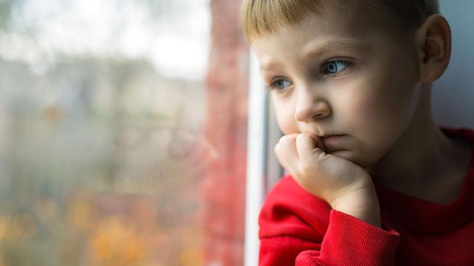 Ein kleiner Junge stützt sein Kinn auf eine Hand und schaut nachdenklich aus dem Fenster.
