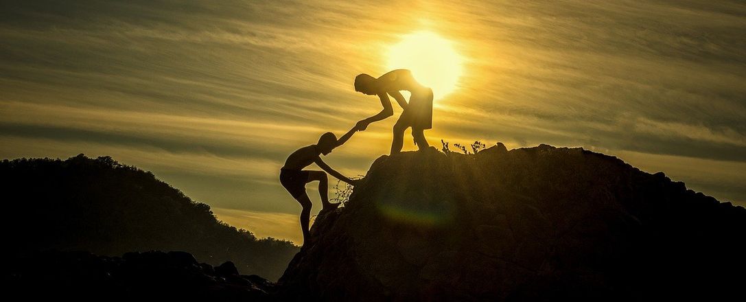 Person hilft anderer Person im Sonnen untergang auf einen Berg